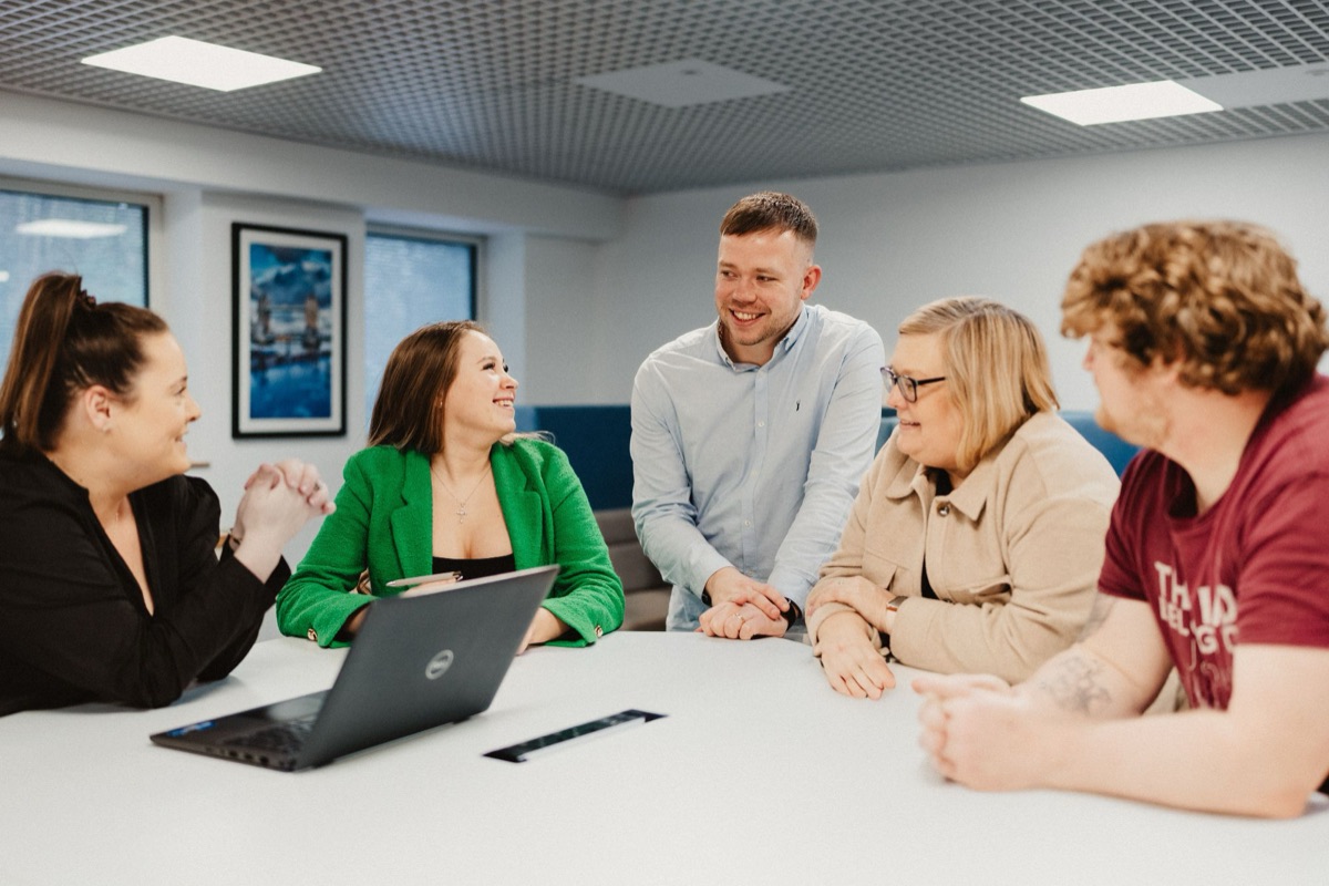 Five members of the Lumina Energy team chatting around a table in the office